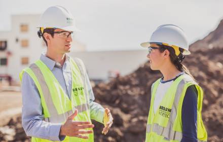 Two employees in hard hats and vests discussing environmental consulting