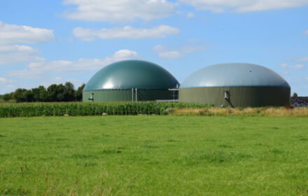 Photo of large green containments for anaerobic digestion. A green lawn is in the foreground and the structures are at a distance against a blue sky with clouds.